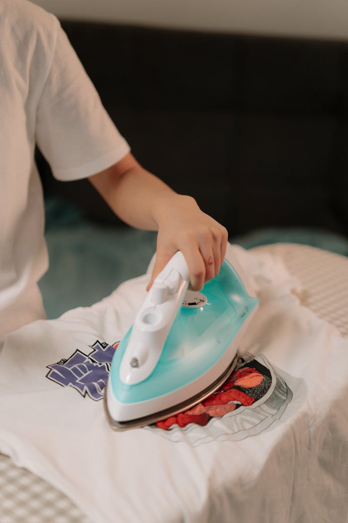 Close-up of a person ironing a graphic t-shirt on an ironing board at home.