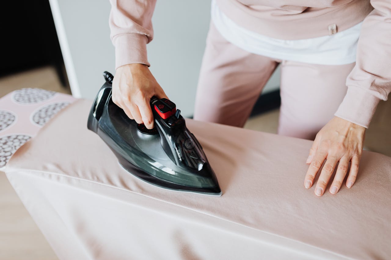 Adult woman ironing clothing on board using a black iron in an indoor setting.
