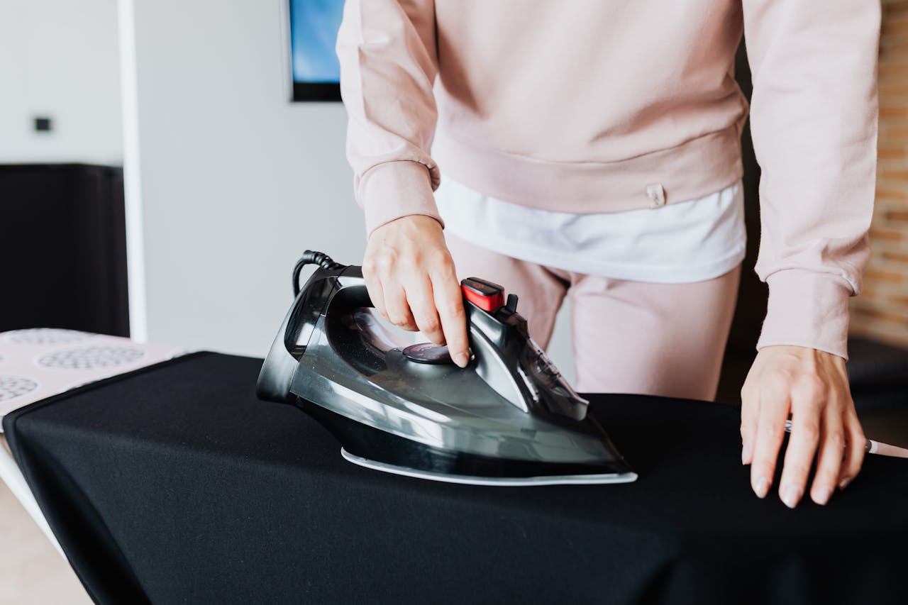 Close-up of a person ironing a black cloth with a modern iron on board indoors.