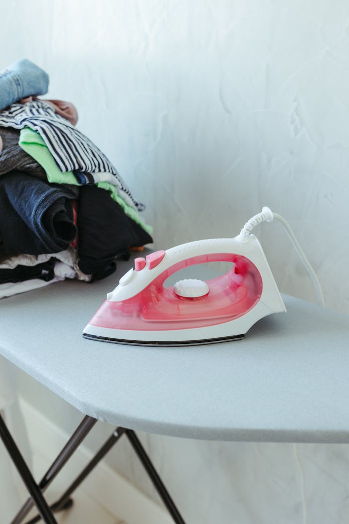 Stack of clothes on ironing board with red and white iron for household chores.